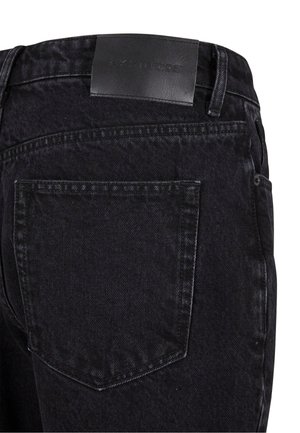 Black denim jeans featuring a textured finish, stitched detailing, and a leather label on the waist with embossed text. Single rear pocket.