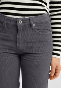 Gray corduroy pants with vertical ribbing, front pockets, and a metal button closure, paired with a black and white striped top.