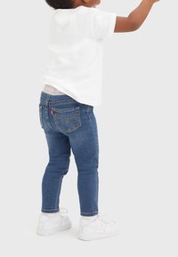 Blå denimjeans med slim fit, med en klassisk design för bakfickor och en vit t-shirt, kompletterad av vita sneakers.