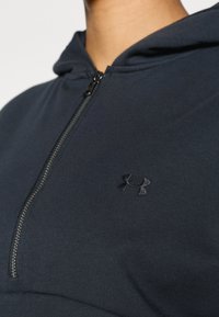 Σκούρο γκρι φούτερ με φερμουάρ στο μπροστινό μέρος μέχρι τη μέση. Διαθέτει  απαλό ύφασμα και μικρό μαύρο λογότυπο Under Armour στο αριστερό στήθος. Σχεδιασμός με κουκούλα.