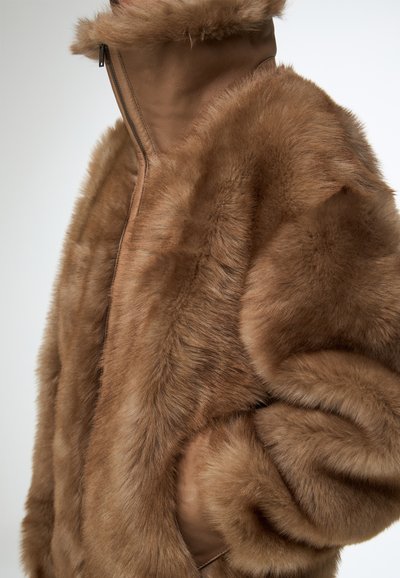 Bruine jas van nepbont met een hoge kraag, een volledige ritssluiting aan de voorkant en zijzakken; een gestructureerde, zachte finish met gladde lederen accenten.