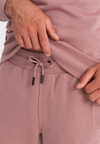 Helle rosa Sweatshirt und Sweatpants mit gerippten Bündchen, Kordelzugverschluss und schwarzen Akzenten. Strukturiertes Material, lockere Passform.