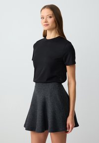 Schwarzes geripptes T-Shirt mit kurzen Ärmeln, kombiniert mit einem grauen, ausgestellten Rock aus weichem Stoff, der eine taillierte Taille und einen glatten Saum hat.
