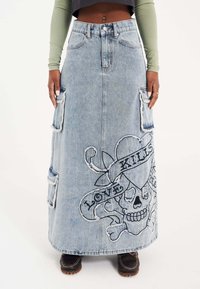 Lysblå denim maxi nederdel med frynset kanter, der har et stort broderet kranie og bannerdesign med teksten "LOVE KILLS."
