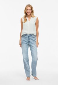 Blusa sin mangas de menta claro con escote en V, combinada con jeans de pierna recta de cintura alta de color azul claro y tacones blancos con tiras.