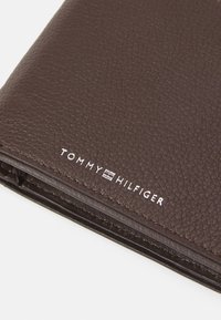 Brown leather wallet featuring a textured finish. White "TOMMY HILFIGER" logo embossed near the bottom edge. Zipper closure visible.