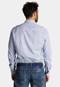 Witte button-up shirt met een klein bloemmotief, voorzien van een achteryoke en plooien. Gecombineerd met blauwe denim jeans en een gestructureerde riem.