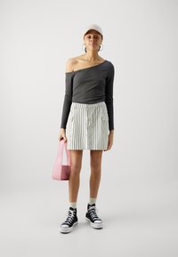 Haut gris à épaules dénudées, jupe rayée, sac rose, baskets noires et chaussettes. Les caractéristiques incluent une texture côtelée, des rayures verticales et un design ajusté.