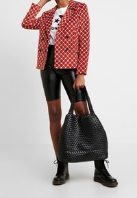 Röd rutig kavaj med en strukturerad design, kombinerad med svarta shorts i konstläder och en vävd svart tote-väska. Svarta snörade kängor.
