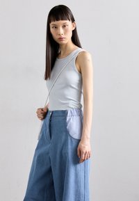 Világoskék bordázott ujjatlan póló, melyet magas derekú, laza farmernadrággal párosítanak, világoskék oldalsó zsebekkel. A modellen egy fonott pántos táska van.