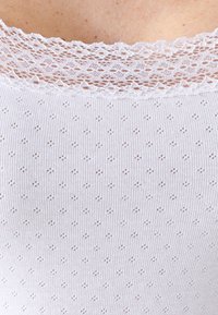 Top sin mangas blanco con un cuerpo acanalado texturizado y un delicado encaje en la parte del cuello, con pequeños patrones de diamantes a lo largo.