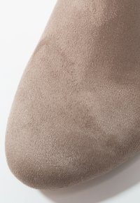 Gros plan sur l'avant d'une chaussure en daim beige, montrant un matériau doux et texturé avec une forme arrondie sur fond blanc.