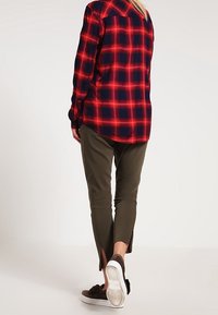 Rood en marineblauw geruite flanellen shirt, olijfgroene, cropped broek met zijsplitten, en bruine instappers met witte zolen.