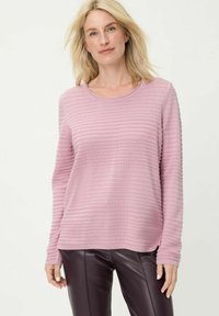 Hellrosa langärmeliger Pullover mit einem strukturierten, gerippten Muster und einem runden Ausschnitt, kombiniert mit dunkelvioletten Lederhosen.
