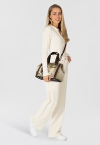 Hellebraune und braune Handtasche mit strukturiertem Design, die eine Materialmischung und ein dekoratives Muster aufweist. Akzente mit goldfarbenen Beschlägen.