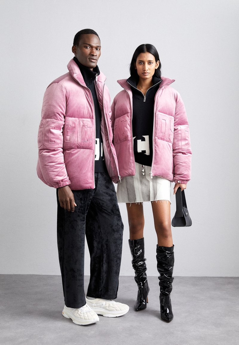 Giubbotti imbottiti rosa con loghi in rilievo, maglioni neri, gonna grigia con orlo sfilacciato, stivali neri lucidi fino al ginocchio e sneakers bianche.