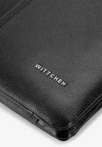 Portafoglio in pelle nera con superficie testurizzata. Presenta il nome del marchio "WITTCHEN" inciso in argento, con dettaglio di cuciture minimaliste.