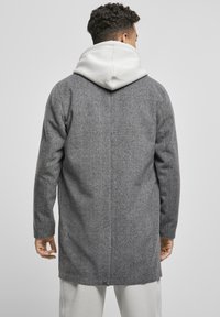 Grå houndstooth-frakke med en mellemlang design. Har en lysegrå hætte under og tekstureret stof for ekstra varme.