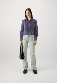 Paars en roze geblokt cropped jack met een ritssluiting aan de voorkant, gecombineerd met lichtblauwe jeans en zwarte schoenen, terwijl ze een zwarte handtas vasthoudt.
