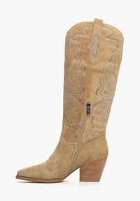 Kawojowe botki z zamszu w kolorze tan, z ostrym toe, skomplikowanymi wzorami haftowanymi oraz srebrnymi ćwiekami. 3-calowy obcas w kształcie klocka. Zapięcie na zamek z boku.