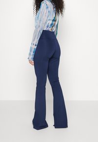 Marinblå utsvängda byxor med en slät textur och hög midja, parat med en blåmönstrad långärmad topp med tie-dye design.