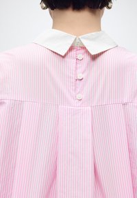 Άτομο που φοράει πουκάμισο με ροζ και λευκές ρίγες και λευκό γιακά, φαινομενικά από πίσω, με τρία κουμπιά στην πάνω πλάτη.