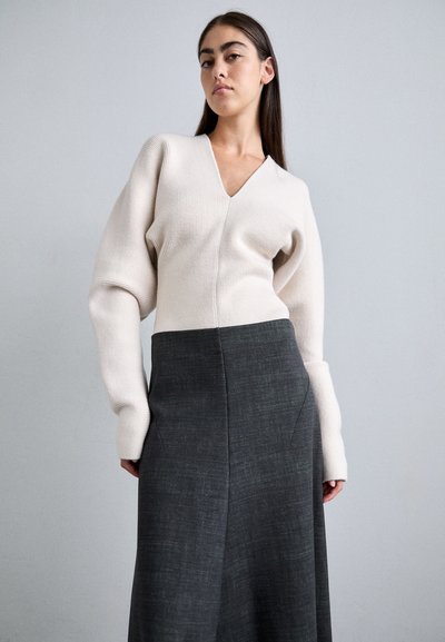 Beige, V-nyakú, kötött pulóver, puffos ujjal, amely sötétszürke, enyhén strukturált, magas derekú szoknyával van párosítva; modern sziluett.