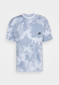 Nike t-shirt in light blue with a dotted pattern, short sleeves, and a zippered chest pocket. Features a crew neck and black logo detail.