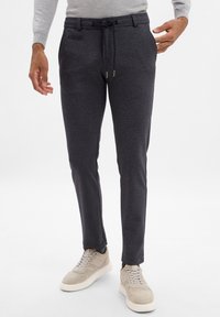 Ciemnoszare spodnie sportowe z elastycznym paskiem, o smukłym kroju i bocznymi kieszeniami, w połączeniu z jasnymi trampkami.