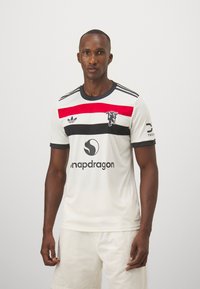 Maglia sportiva bianca con strisce rosse e nere, colletto tondo, maniche corte, con il logo Adidas e il branding Snapdragon sul davanti.