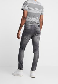 Jeans gris de corte slim con detalles desgastados y múltiples bolsillos, combinados con una camiseta de rayas gris y zapatillas blancas.