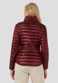 Veste matelassée rouge avec un col haut et des coutures horizontales. Le matériau est brillant et léger, épousant étroitement le corps.