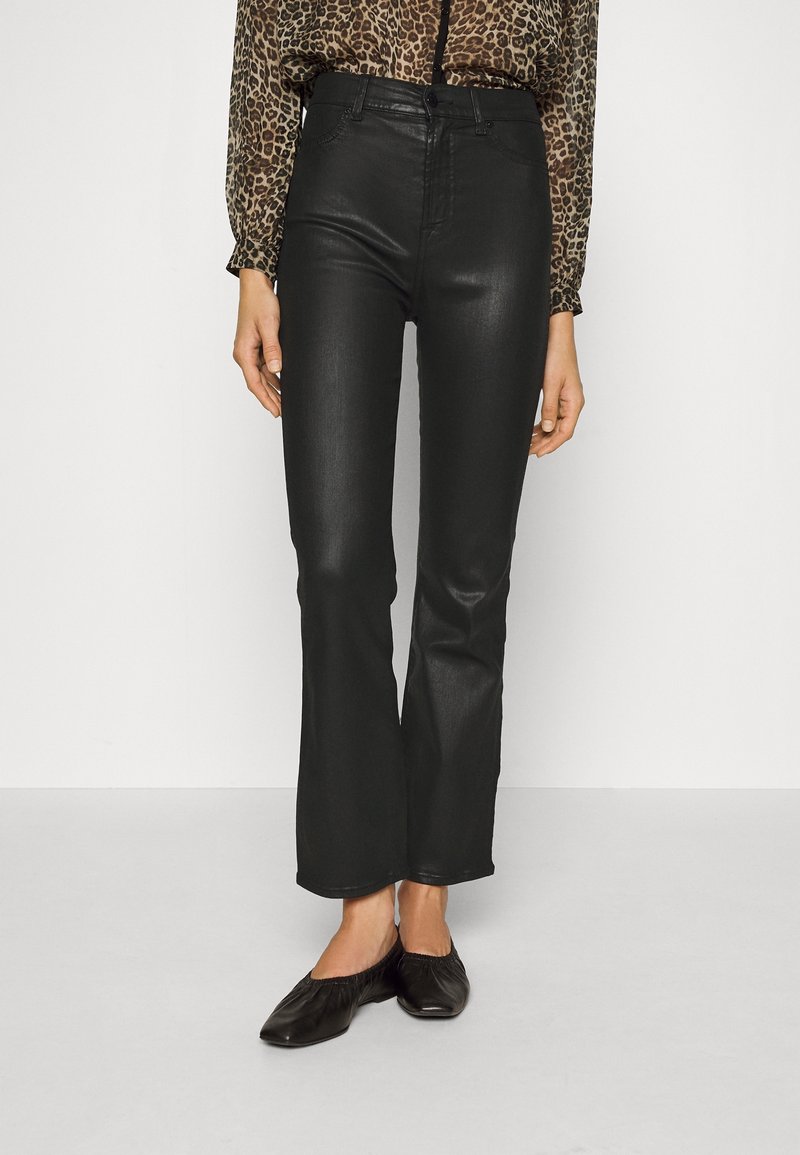 Pantalones vaqueros acampanados de imitación cuero negro con una cintura alta, que presentan una textura suave y un ligero brillo, combinados con zapatos planos negros.