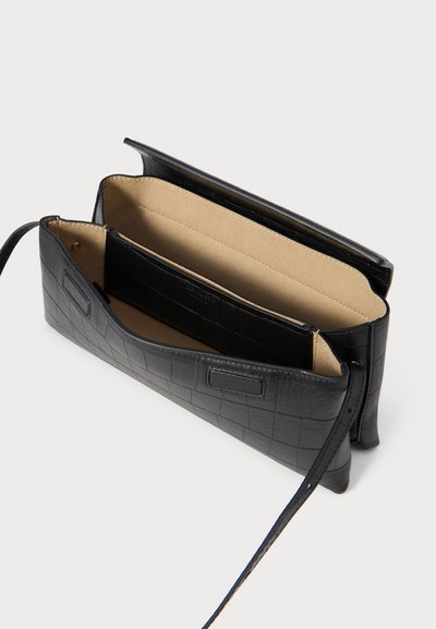 Bolso de cuero negro con estampado de cocodrilo y acabado suave, con compartimentos interiores y una correa ajustable. Se abre por la parte superior.