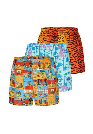 Gespiereerde man met korte vlechten, die lichtblauwe boxershorts met kleurrijke dinosauruspatronen draagt, staand tegen een effen lichte achtergrond.