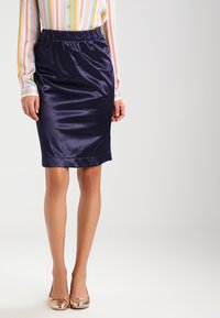 Jupe crayon en satin bleu marine avec une taille élastique, texture lisse et design au genou, associée à un chemisier à rayures colorées.