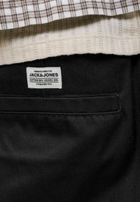 Μαύρο παντελόνι με ραμμένη ετικέτα Jack & Jones πάνω από την πίσω τσέπη, συνδυασμένο με μπεζ ριγωτή και καφέ καρό πλεκτή στρώση πάνω από τη μέση.