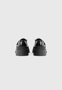 Chaussures à plateforme noires avec une finition brillante, dotées de semelles épaisses et d'accents en métal argenté. Le design a une forme arrondie avec des sangles ajustables.