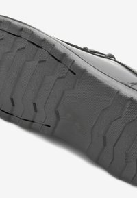 Semelle de chaussure en caoutchouc noir avec une surface texturée présentant des motifs de semelle prononcés pour une adhérence et une stabilité, vue en angle du profil latéral.