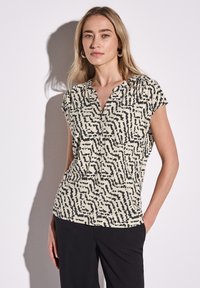 Blusa a maniche corte color crema con un motivo astratto nero. Presenta un design senza colletto e un tessuto morbido e leggero.