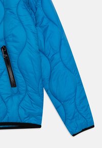 Giacca blu trapuntata con finitura lucida, tasca con zip, dettagli con zip nera e polsini elastici con orlo nero a contrasto.