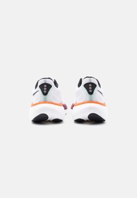 Ζευγάρι λευκών αθλητικών παπουτσιών με μαύρες λεπτομέρειες και πορτοκαλί επένδυση, εμφανιζόμενα από πίσω σε απλό ανοιχτό γκρι φόντο.