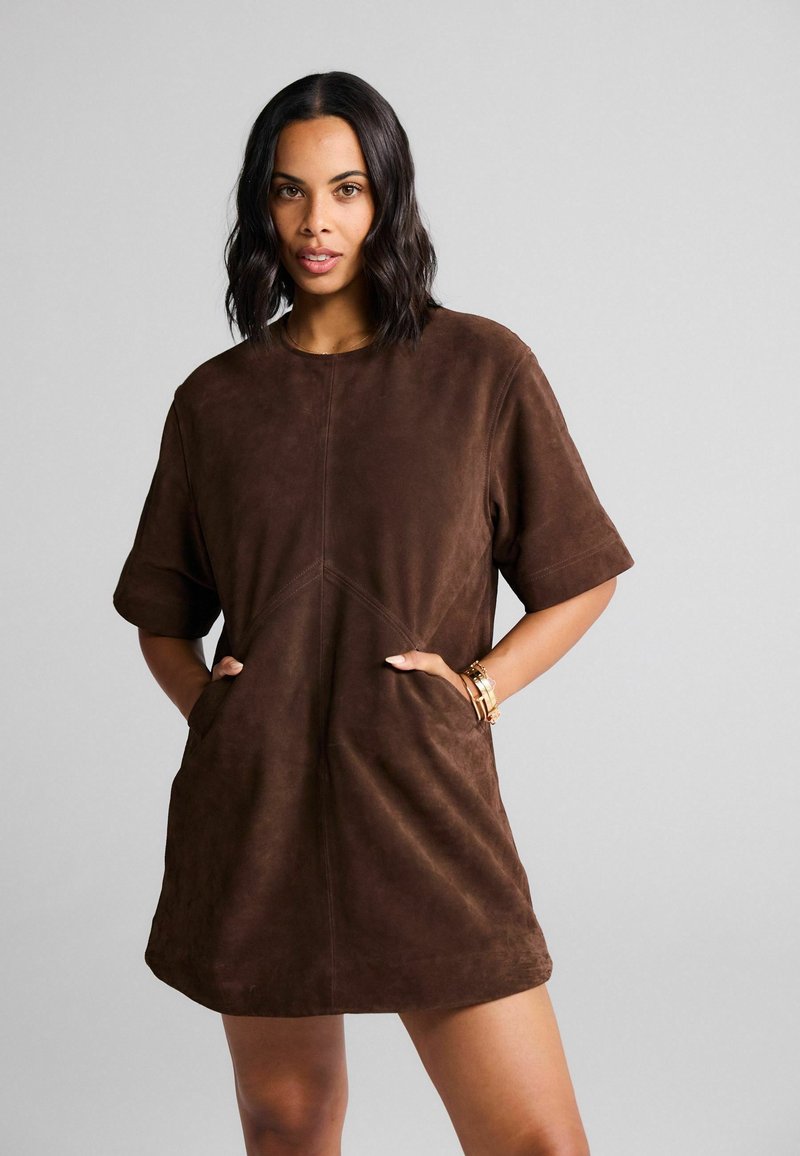 Robe mini en suédine marron avec des manches courtes, un col rond et des poches avant. Présente des détails de couture pour un design structuré.