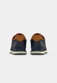 Blue and burgundy sneakers with a tan heel, featuring a textured finish, rubber sole, and “New Balance” branding on the back.
