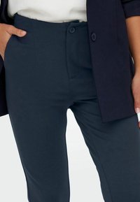 Mörkblå skräddarsydda byxor i en slät tygkvalitet, med dragkedja, två sidofickor och en figursydd design för en ren silhuett.