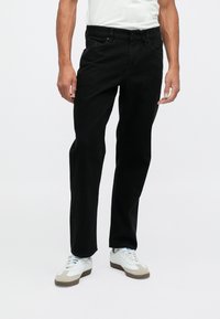 Vaqueros de mezclilla negra con corte recto, diseño de cinco bolsillos y cierre de botón. Combinados con zapatillas blancas, mostrando un estilo informal.