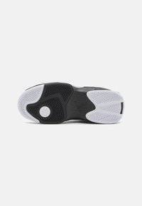 Czarna podeszwa sportowego buta z teksturowanymi wzorami, z białym akcentem na czubku i okrągłym logo osadzonym w centrum.