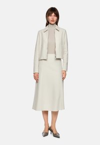 Cream two-piece outfit featuring a structured cropped jacket and a fitted skirt, made of textured fabric. Complemented by gray heels.