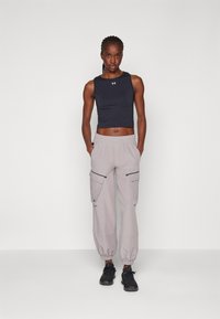Top corto senza maniche nero, pantaloni cargo grigi con polsini elasticizzati, due tasche con cerniera e scarpe sportive nere. Sfondo semplice.