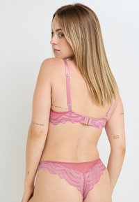 Ensemble soutiens-gorge à dos en dentelle et culotte assortie en rose pâle, avec bords festonnés, bretelles réglables et détails en dentelle délicate.